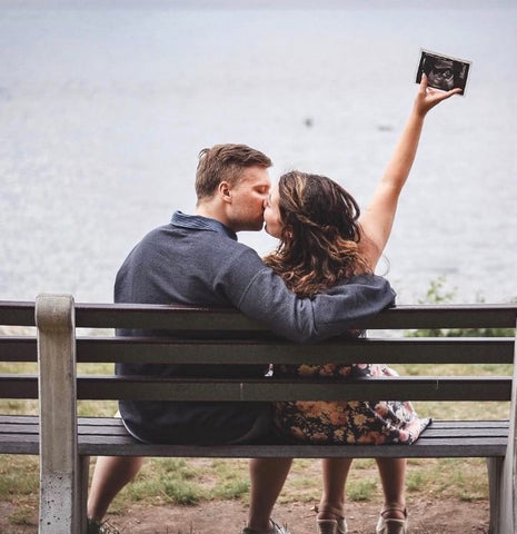 Couple poses with an ultrasound on a park bench