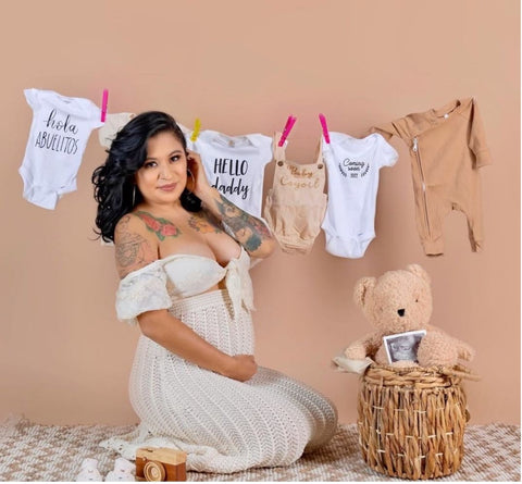 Pregnant woman poses with onesies on a clothesline to announce a pregnancy