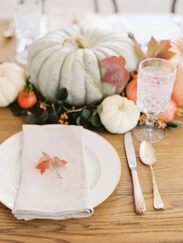 Table setting featuring pastel pumpkins, plus and a small leaf on a folded white napkin for a fall baby shower