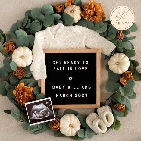Baby onesie arranged with letterboard and fall-themed wreath to announce pregnancy