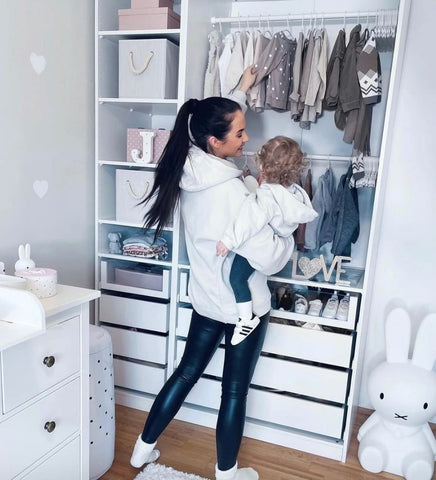 Mom and toddler looking at clothing hanging in an open closet.