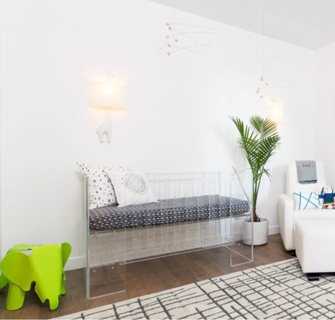 White nursery with a clear acrylic crib, graphic rug, and pops of bright colors