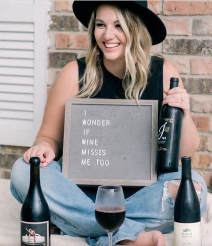 Woman holding a bottle of wine and letterboard that says "I wonder if wine misses me too"