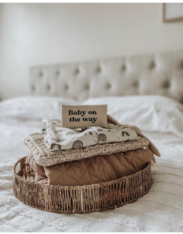 A pile of folded blankets and sweaters with a sign on top that says "Baby on the Way"