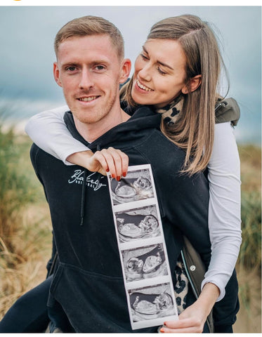 A couple wears hoodies and holds a sonogram photo in a winter pregnancy announcement