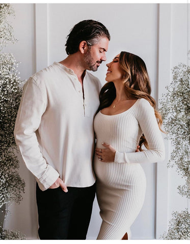 A couple poses indoors near a holiday tree in a winter pregnancy announcement