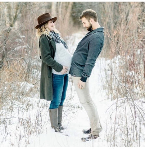 A couple poses in the snow to announce a winter pregnancy