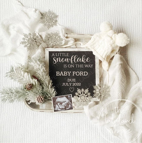 A winter pregnancy announcement styled with snowflakes, winter branches, and white baby knits