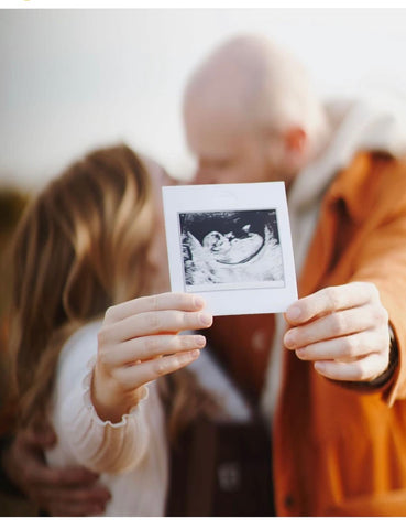 A couple kisses and holds a sonogram photo in a winter pregnancy announcement