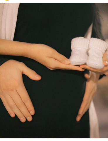 A couple poses with a pair of knit baby booties in a winter pregnancy announcement