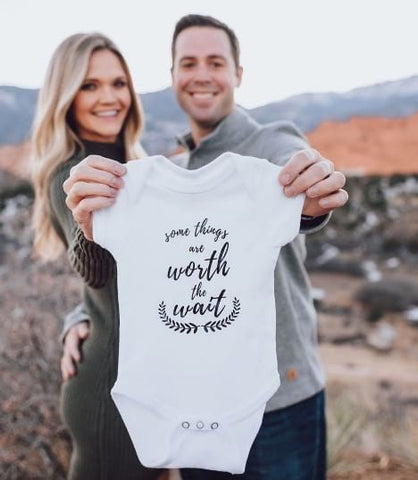 Couple holding onesie that says "Worth the wait"