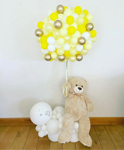 Giant teddy bear holding yellow and white balloons