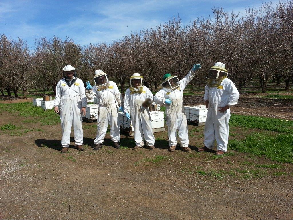 five beekeepers in full protective gear doing a silly pose outside