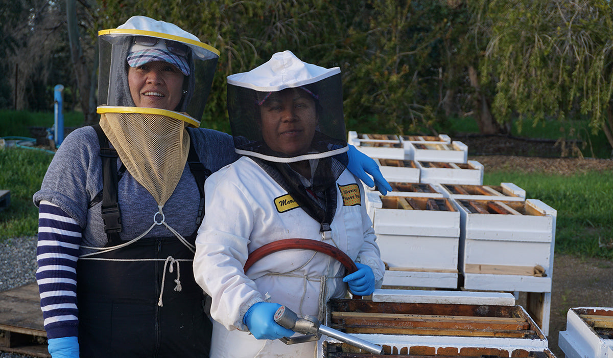 two female beekeepers smile for the camera while at work
