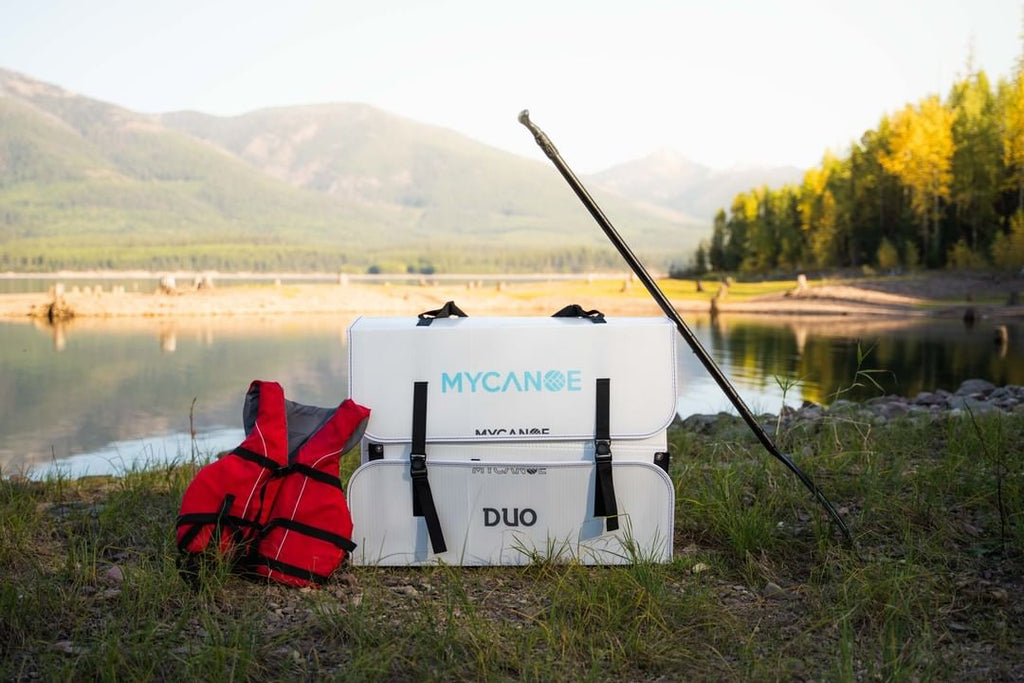 foldable fishing canoe with life jacket and paddle in front of a lake and mountain