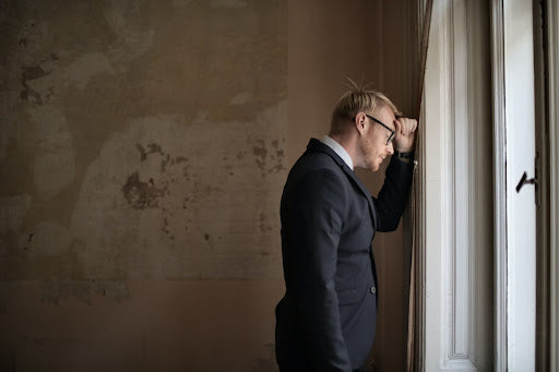 Man in a blazer looking stressed with his hand against a wall near his head