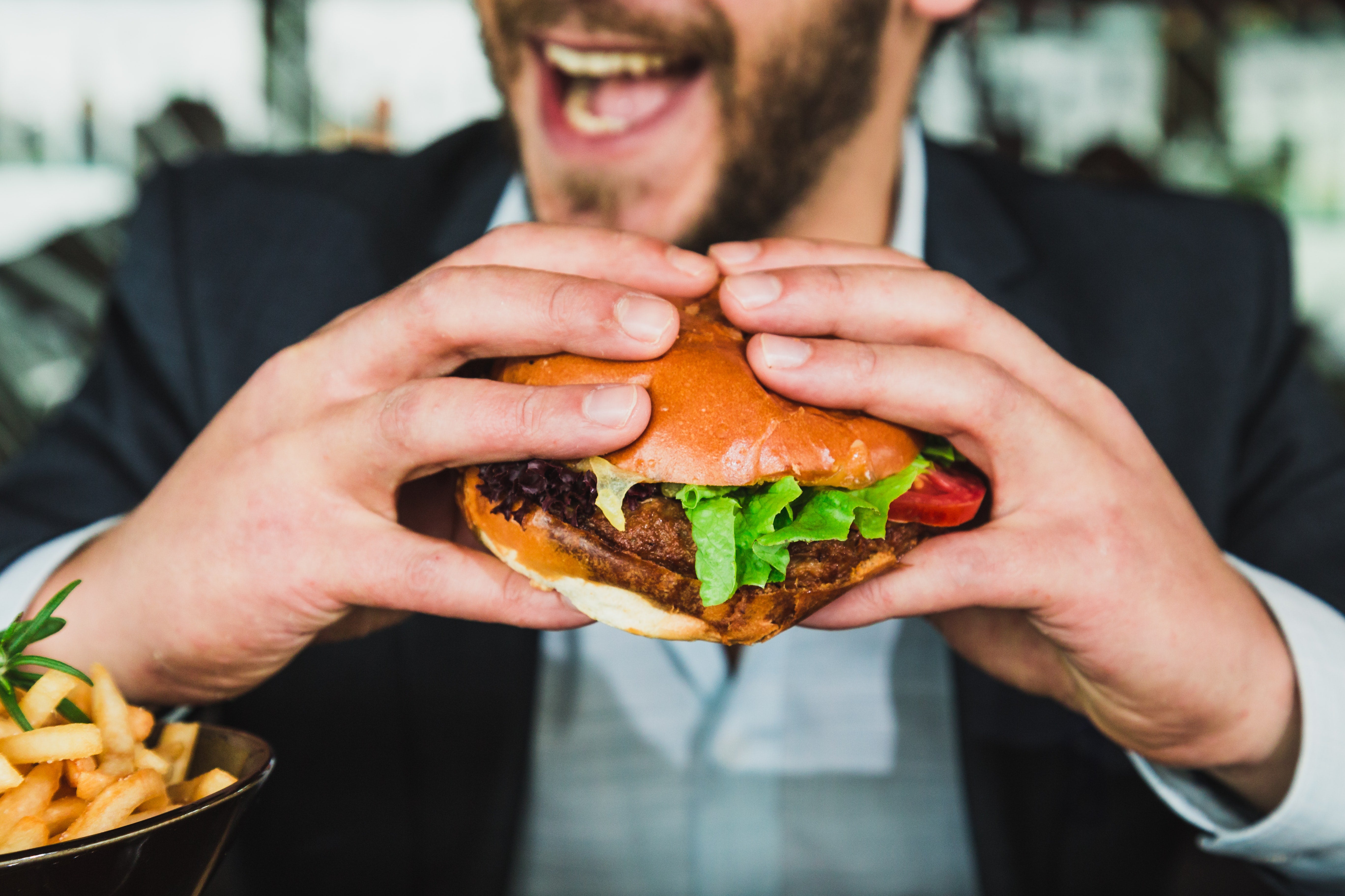 zoomed in image of a burger being eaten by a man who is smiling