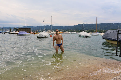 Man in black briefs and sunglasses on the sandy shores of a river