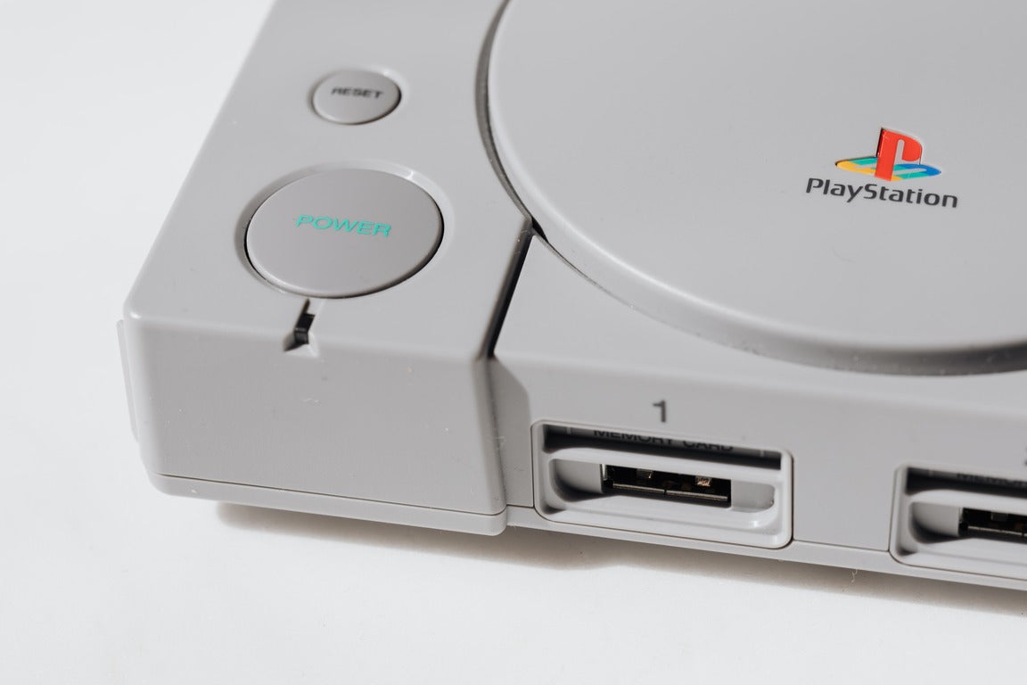 Grey sony playstation with a joystick against a white background 