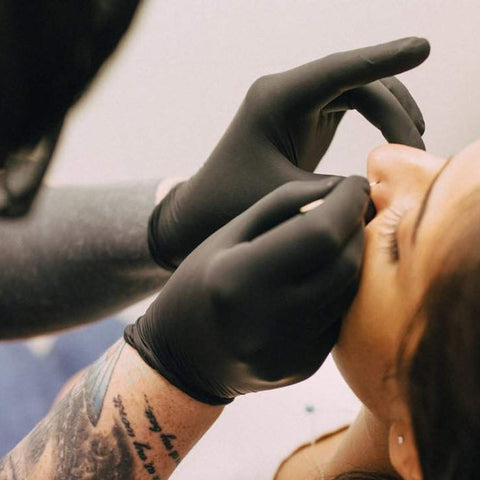 A piercer using a piercing needle to do a nose piercing