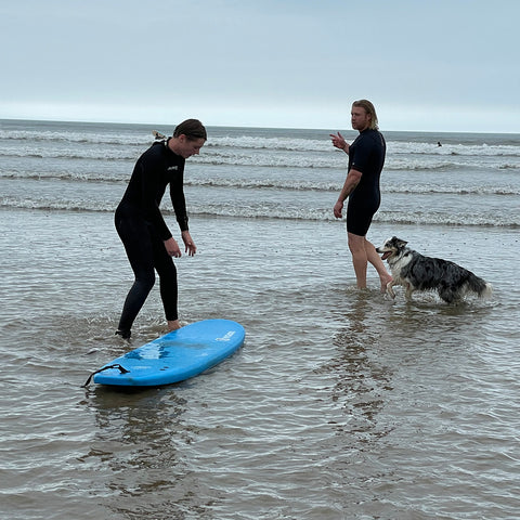 Ben and Ollie standing in the surf with Willow the collie dog looking on