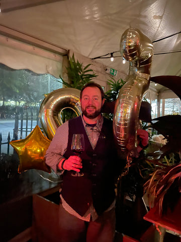 Man standing with his 50th birthday balloons in a restaurant.