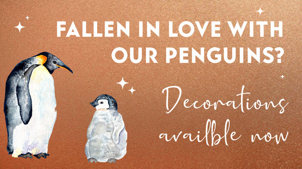 Two realistic watercolours of adult and chick Emperor Penguins on a copper background with white stars dotted around. The caption reads "Fallen in love with our penguins? Decorations available now"