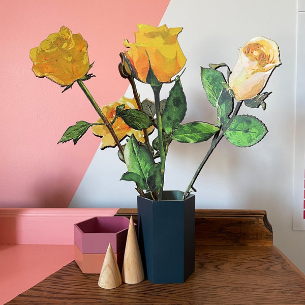 bunch of yellow wooden roses, all different, displayed in a dark blue hexagonal vase