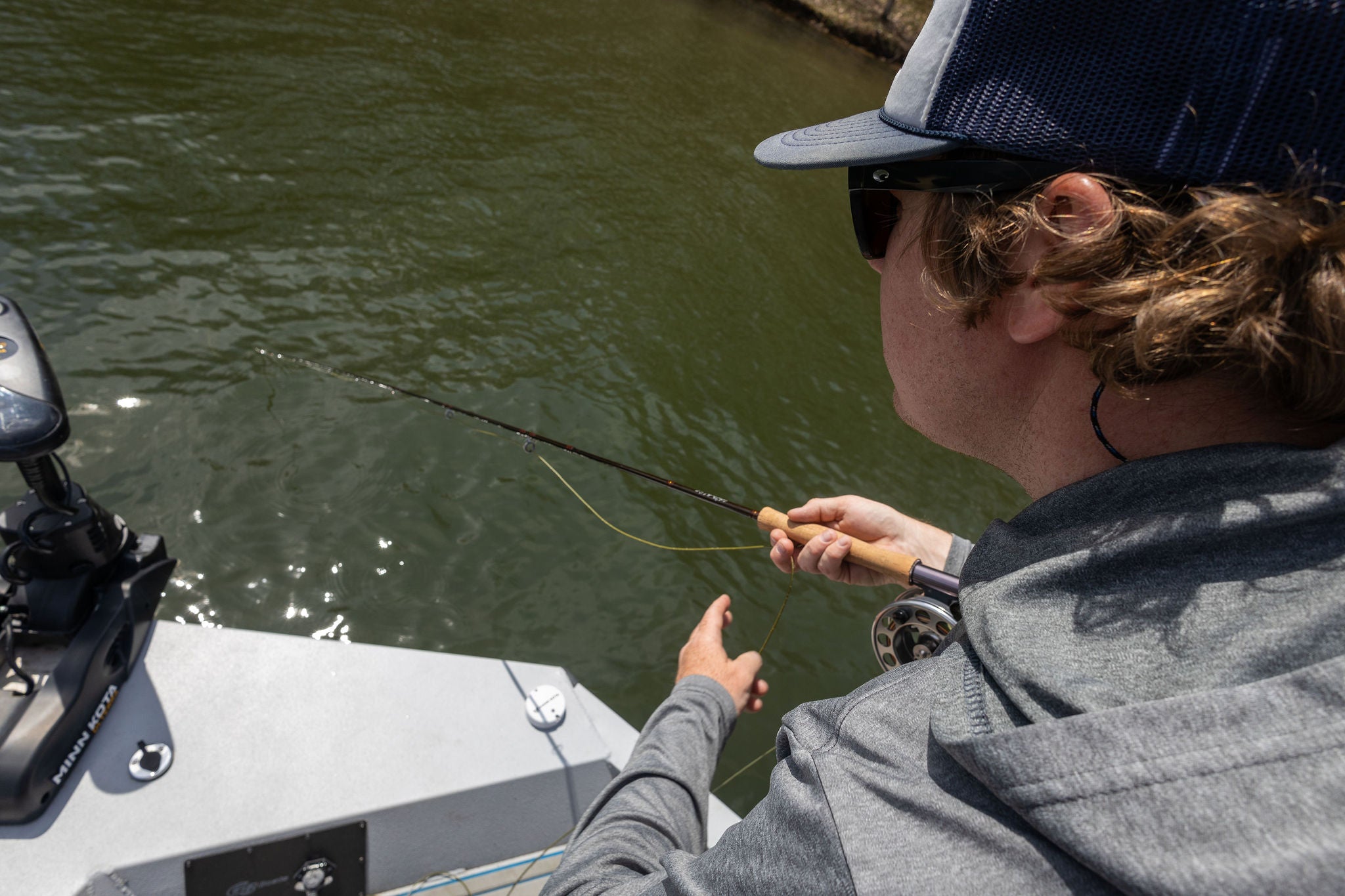 A fisherman is standing on the stern of a boat and fly fishing