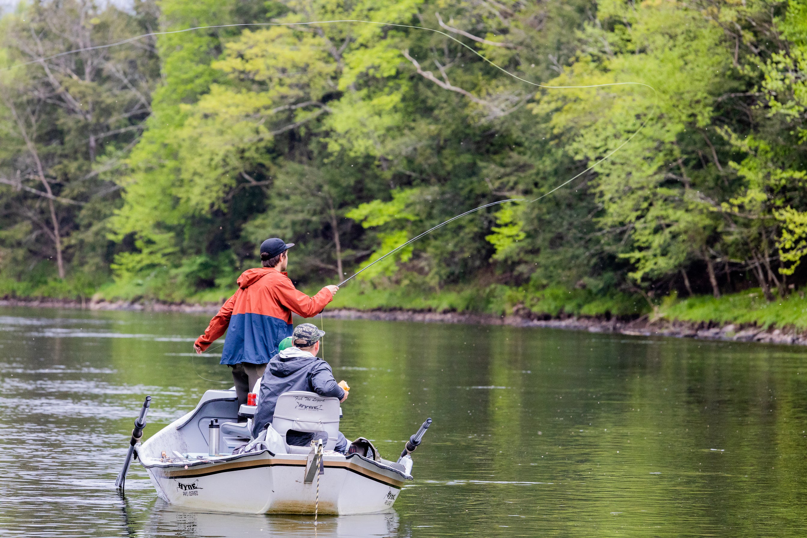 Three fishermen on a boat and one is casting out his line