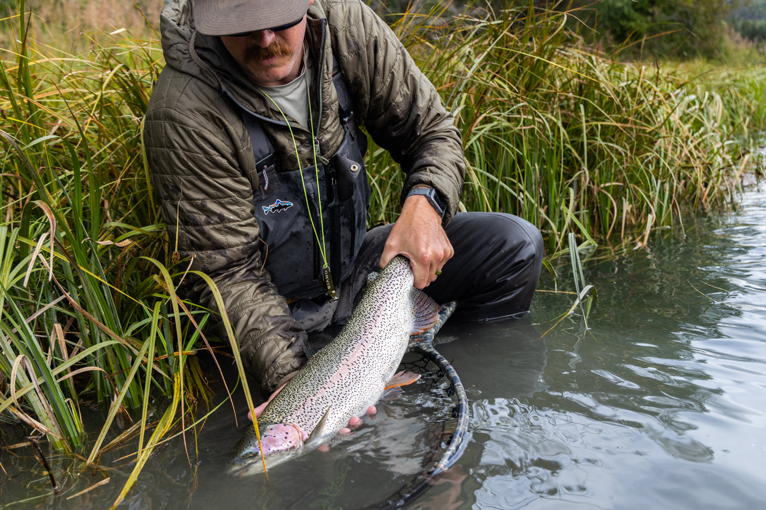 A man kneeling down and holding onto a fish in shallow water