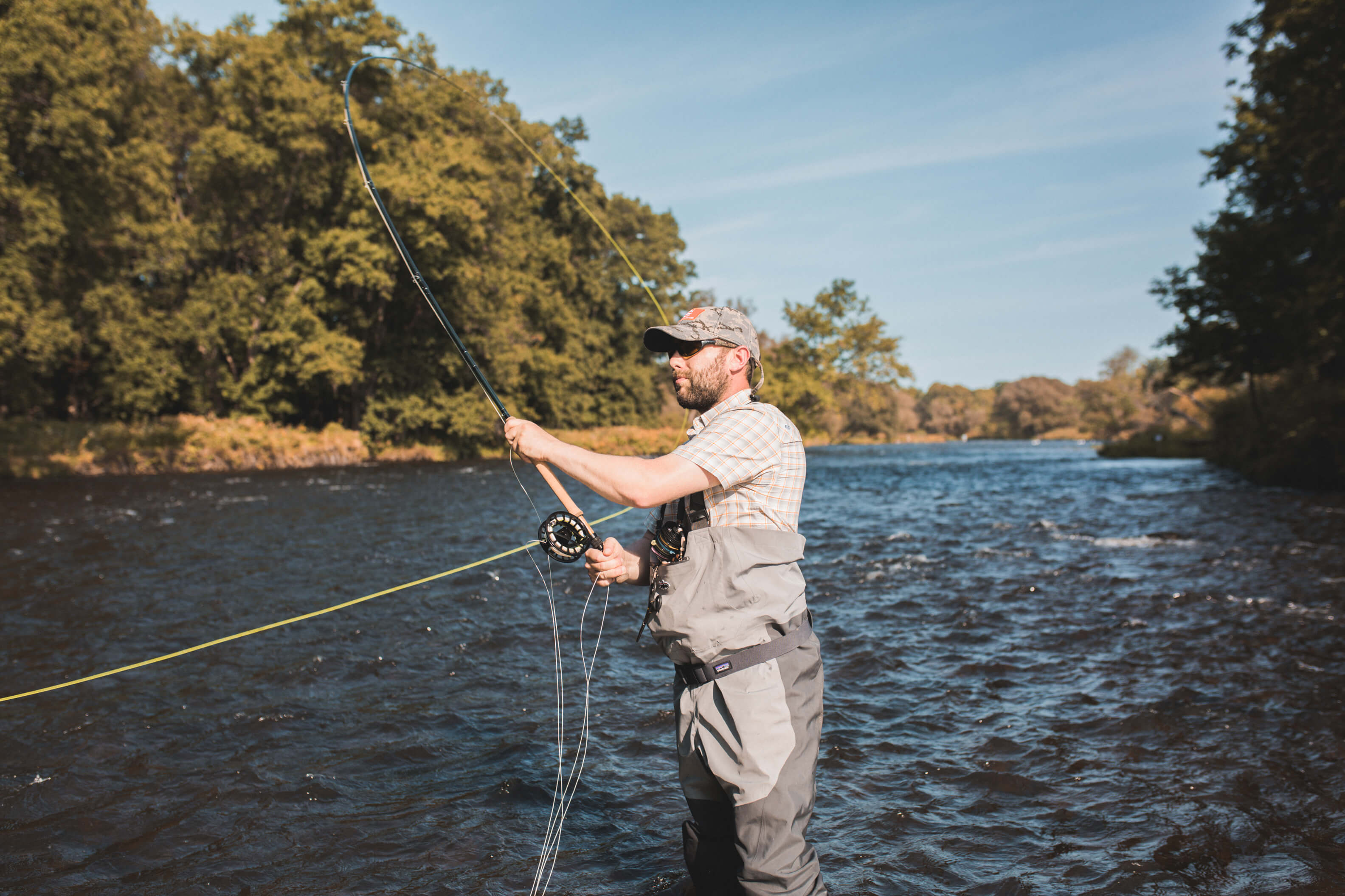 Brooks pesca con mosca en el río Salmon. Está parado en el agua hasta las rodillas y está a punto de lanzar su línea.