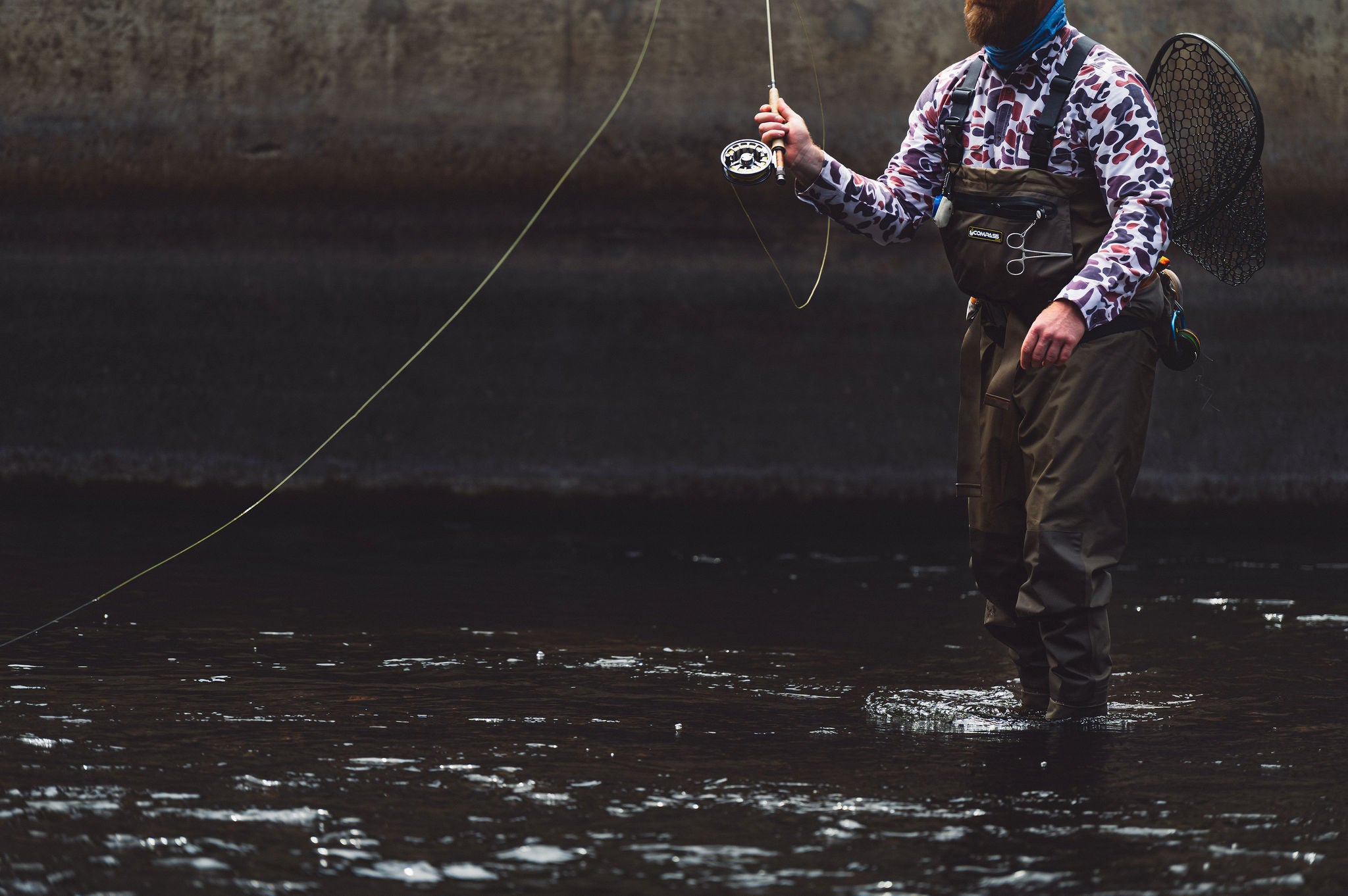 A man standing in ankle high water and casting his fly fishing line