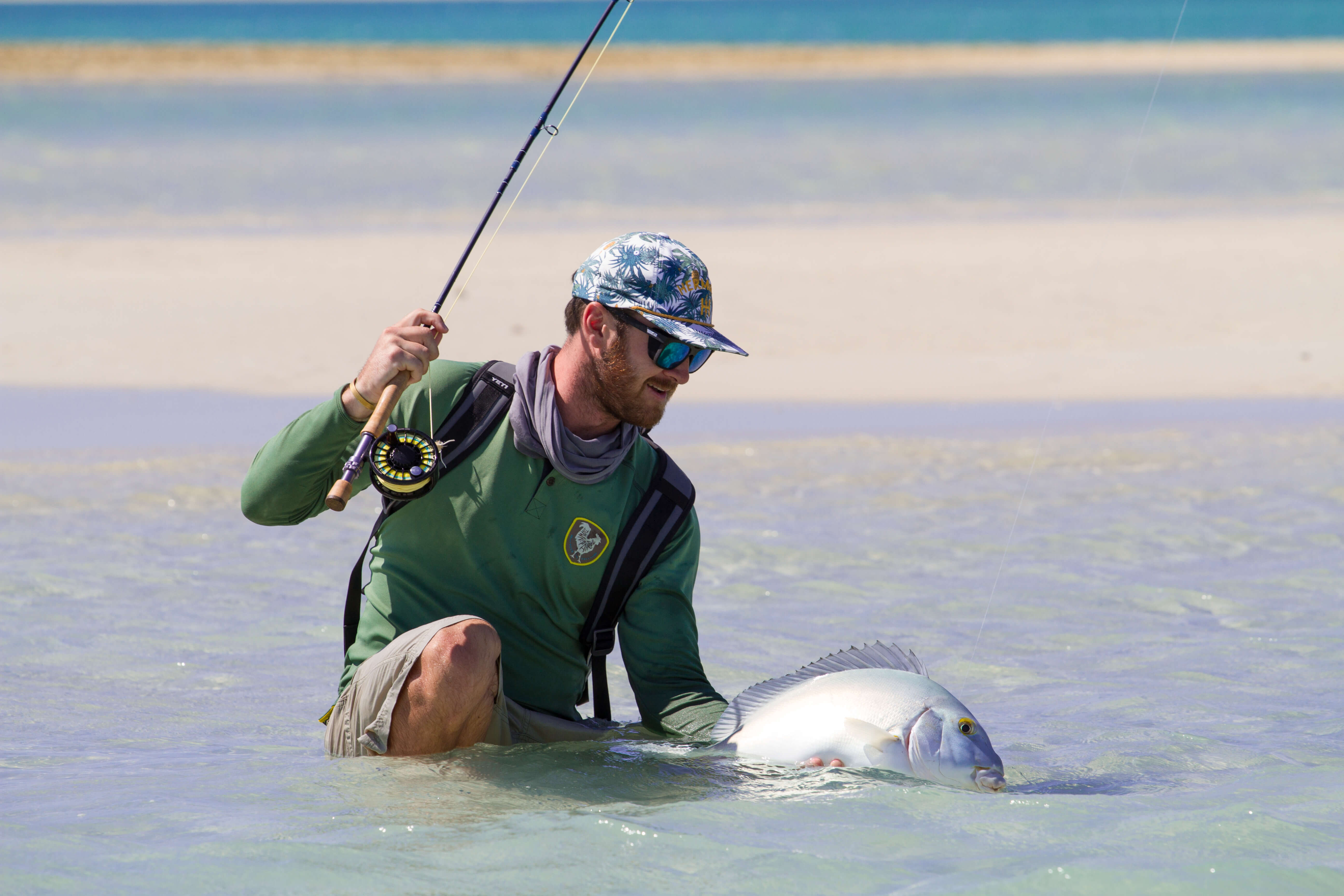A fisherman kneeing in water holding his fly fishing rod and a fish he caught