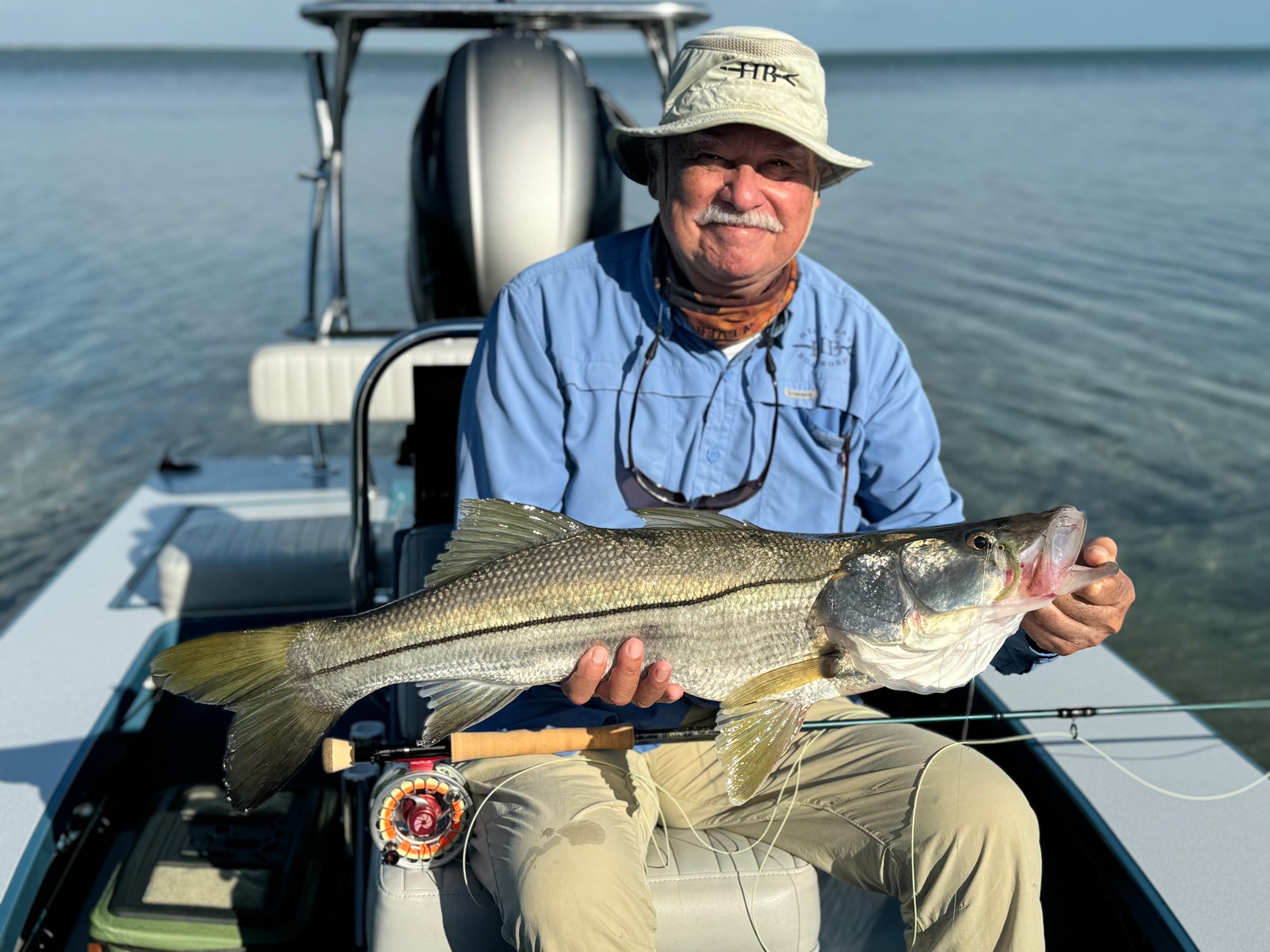 A fisherman is seated on a boat and holding up a fish