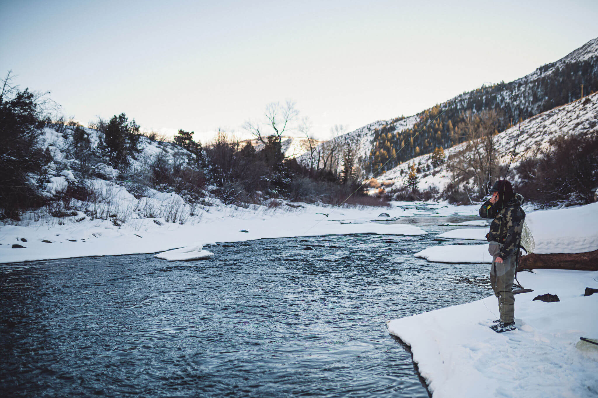 Angler fishing during the winter on the banks of a river while reeling in his fly line