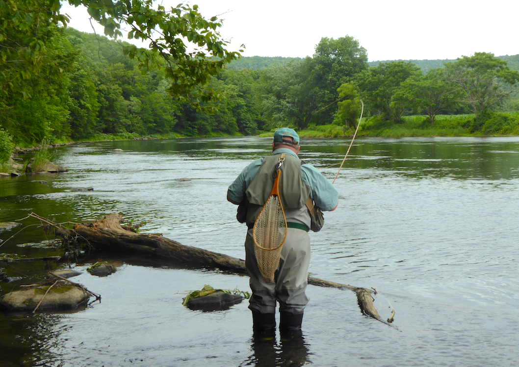 John Shaner steht in einem niedrigen Bach und fischt mit dem Rücken zur Kamera Fliegenfischen