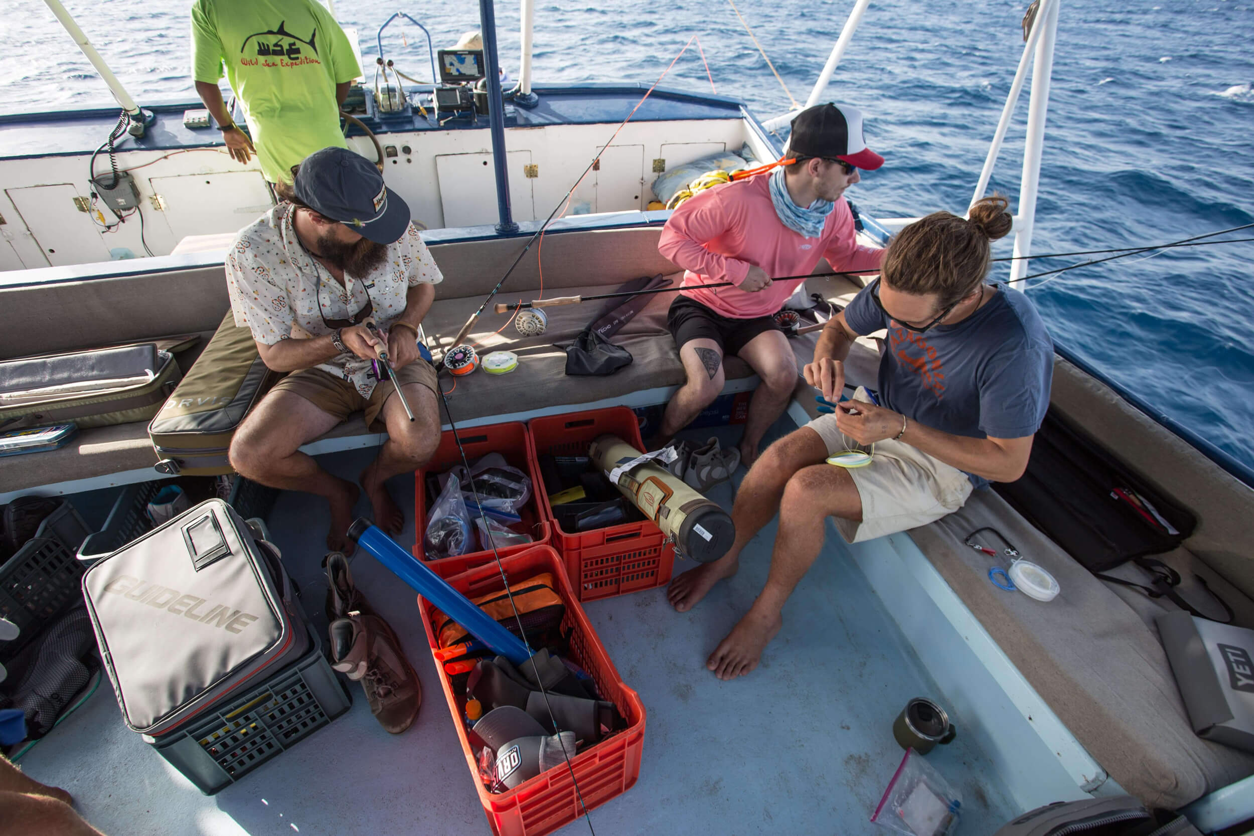 Tres hombres en un barco inspeccionando sus líneas y carretes de pesca con mosca