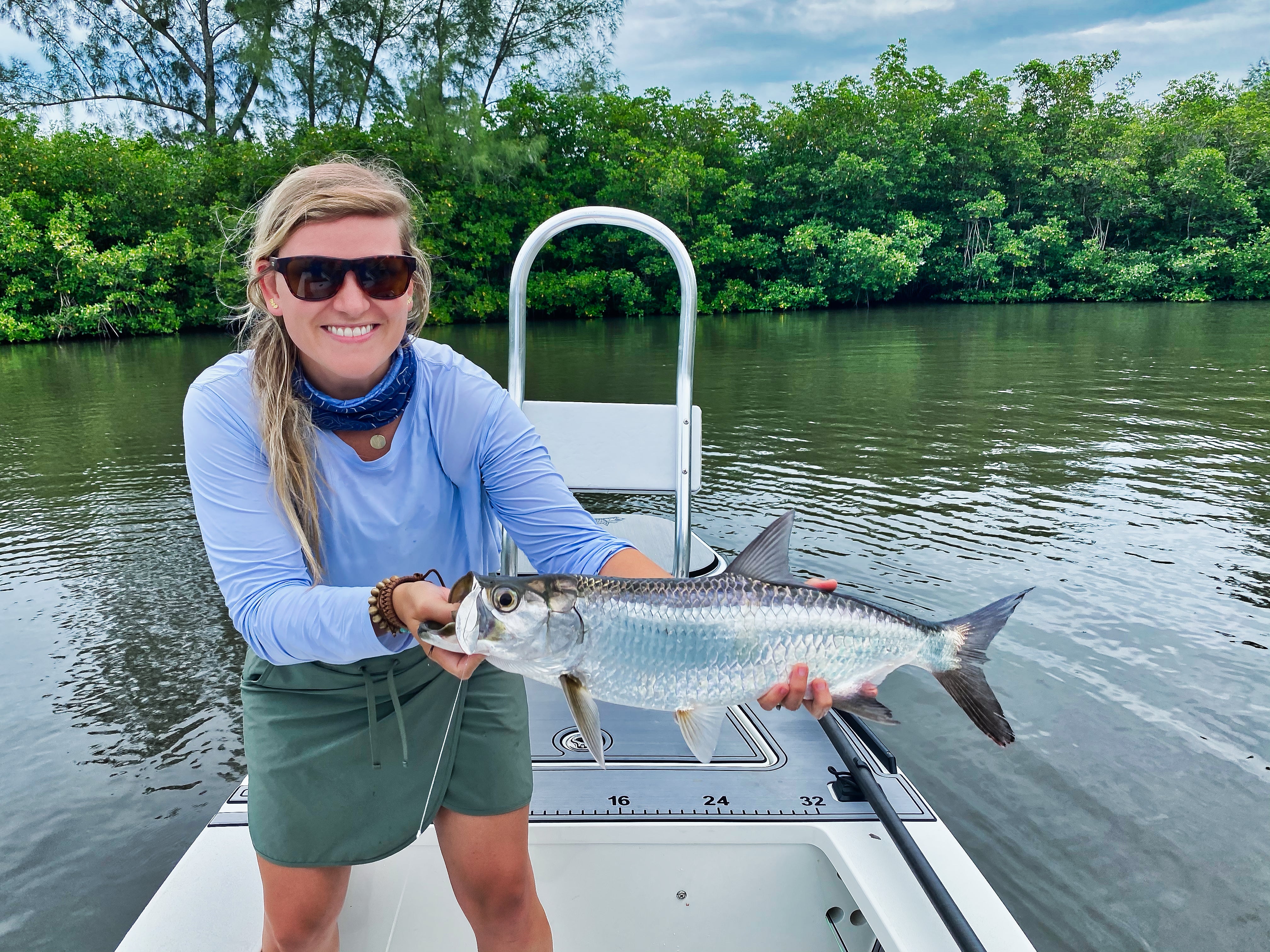 Woman on a boat holding up a tarpon she caught