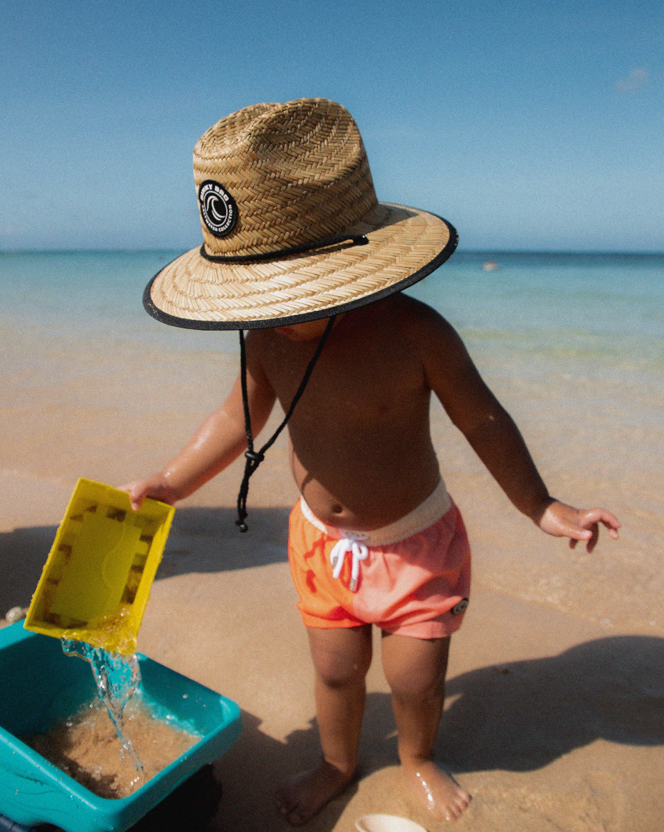 baby playing with sand in a binkybro swimsuit and sunhat