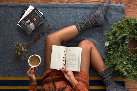 A woman lounging and reading a book while drinking coffee.