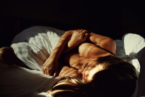 A woman wearing a sleep bra in bed with arms crossed and the sun coming in through the window.