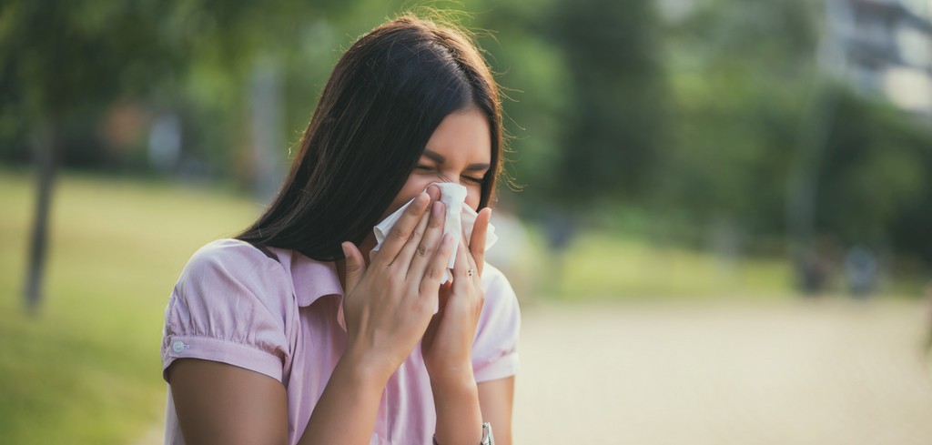 Woman outside in park sneezing into tissue