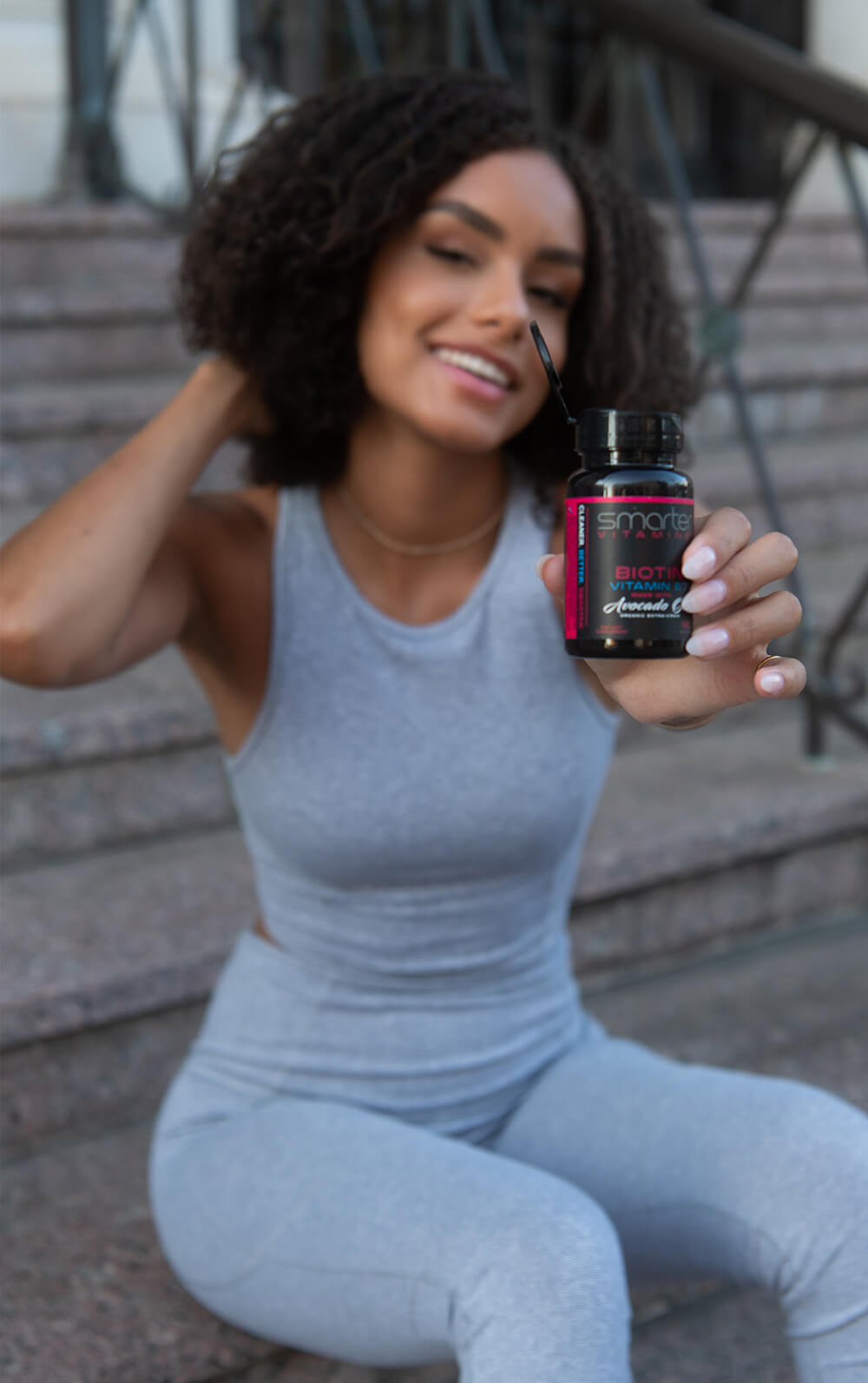 Woman holding smarter biotin bottle touching hair and smiling