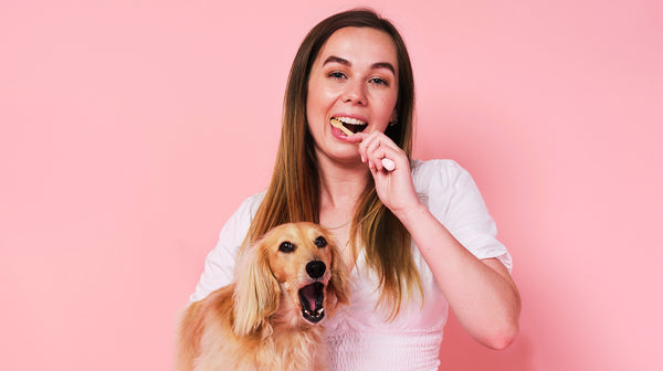 A woman with dark hair holding her golden puppy, brushing her teeth