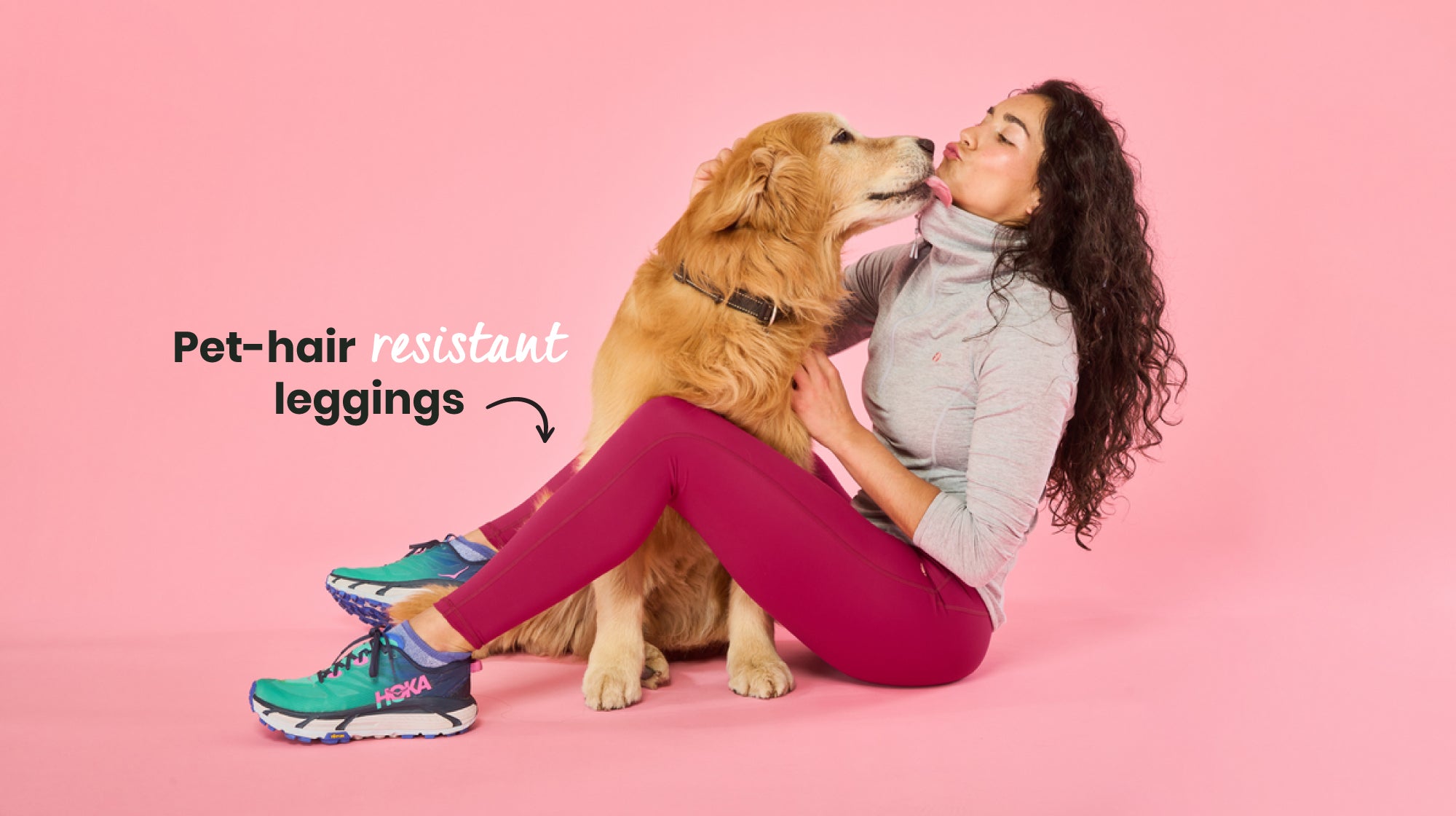 Woman cuddling golden retriever dog, wearing ACAI pet-hair resistant leggings, against a pale pink background