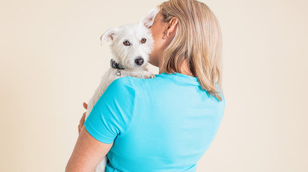A woman with short blonde hair, wearing a bright blue t-shirt, cuddling her white dog