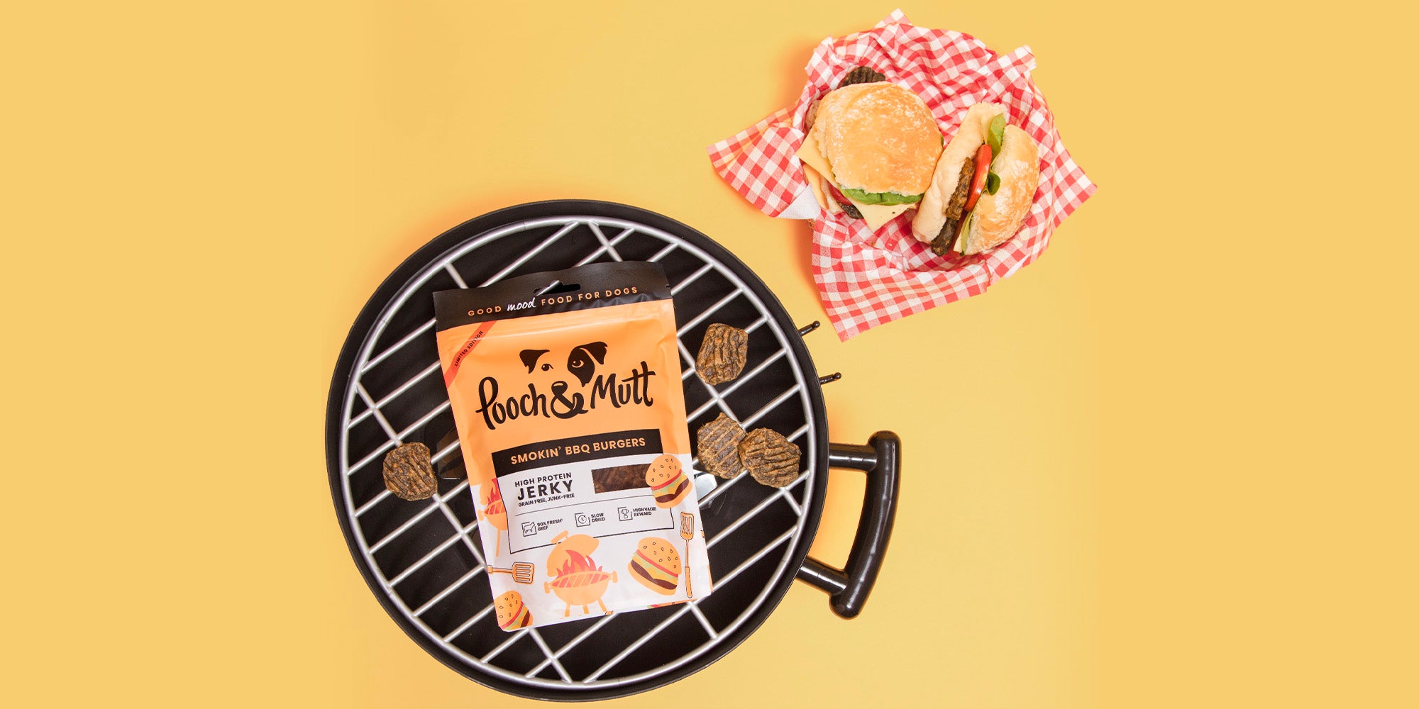 An unlit BBQ with Pooch & Mutt Somkin' BBQ Treats in bag on it, against orange background