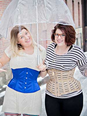 friends side by side sharing an umbrella, one in the blue satin Modern Curve Underbust Corset CS-411 and the other in a beige mesh Hourglass Curve Longline Underbust Corset CS-426