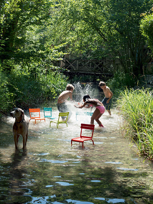 children playing in creek with colorful fermob chairs